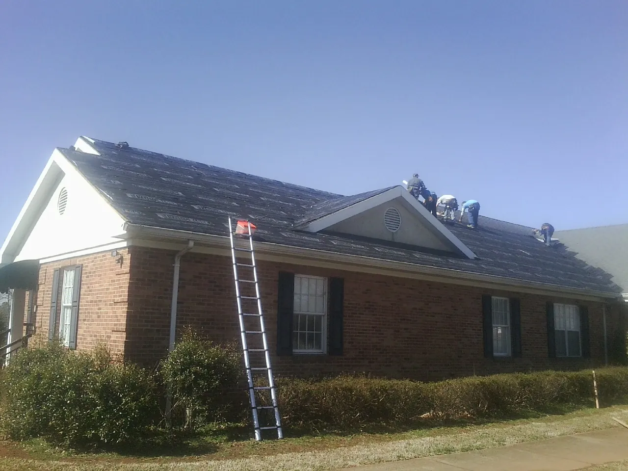 Crew tearing shingles off a brick ranch roof with a ladder set — Emergency Roof Repair work by our crew in Sherrills Ford