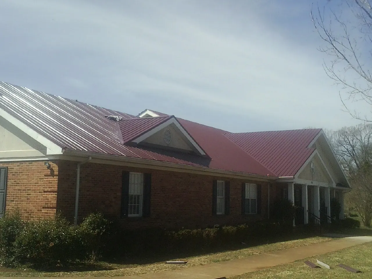 Red metal roof with gabled entries on a long brick building, from a Hail Damage Roof Repair job in Sherrills Ford