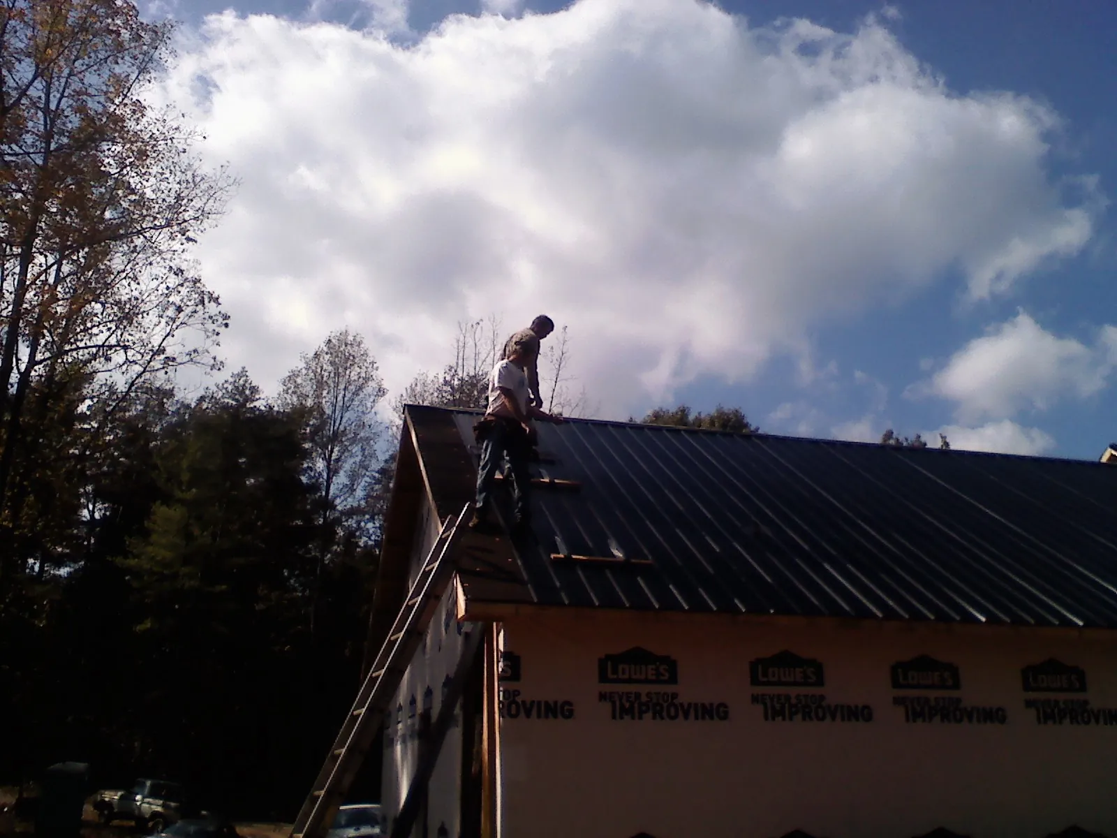 Roofer fastening dark metal panels high against a cloudy sky, from a Roof Inspection job in Sherrills Ford