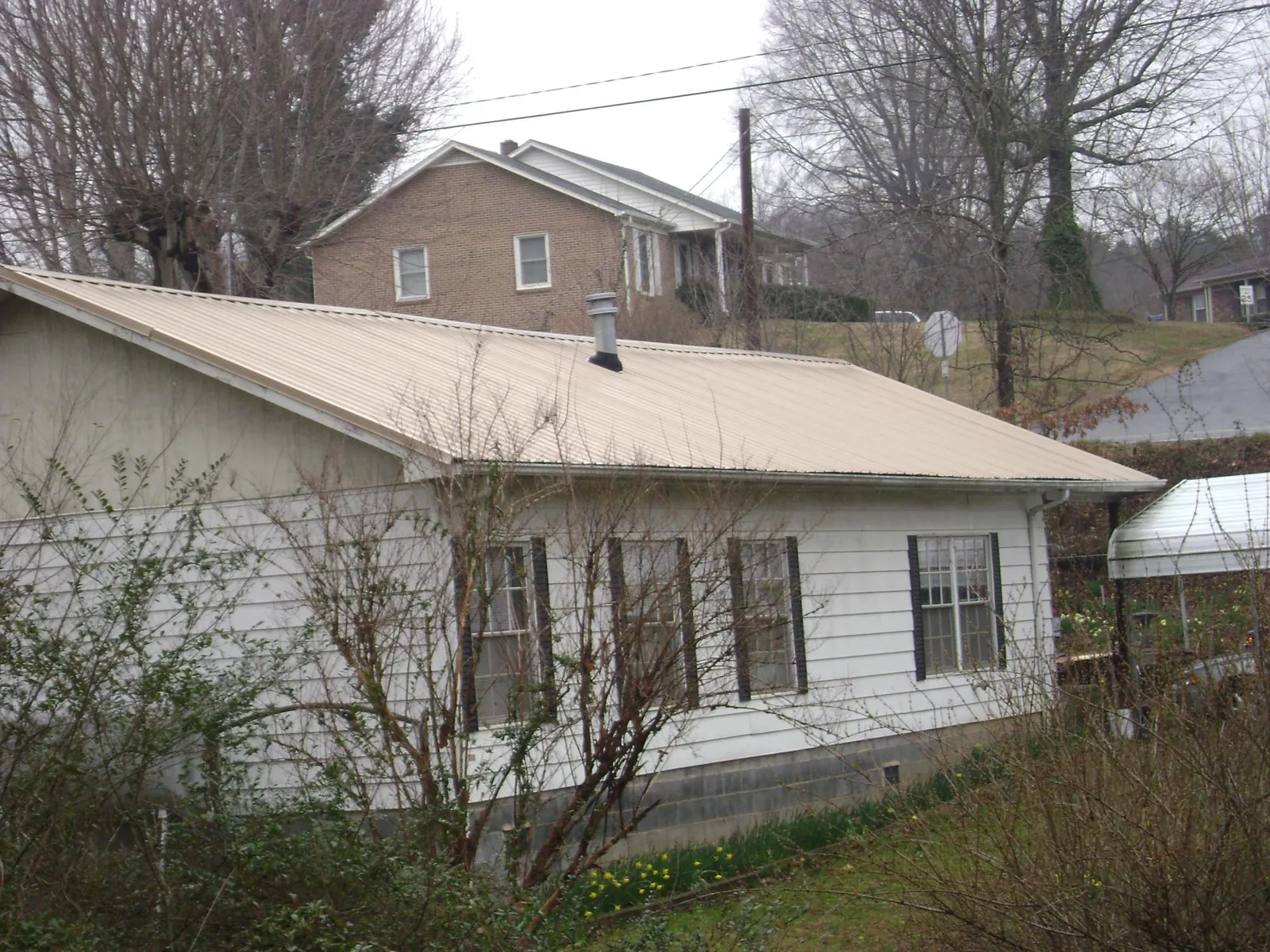 Tan metal roof on a white sided house set into a hillside in Sherrills Ford